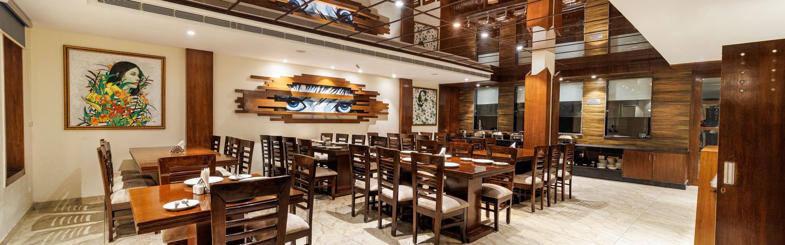 Restaurant at Inde Reva Resorts Rishhikesh featuring wooden furniture, open ceiling design, framed art, and tiled flooring.