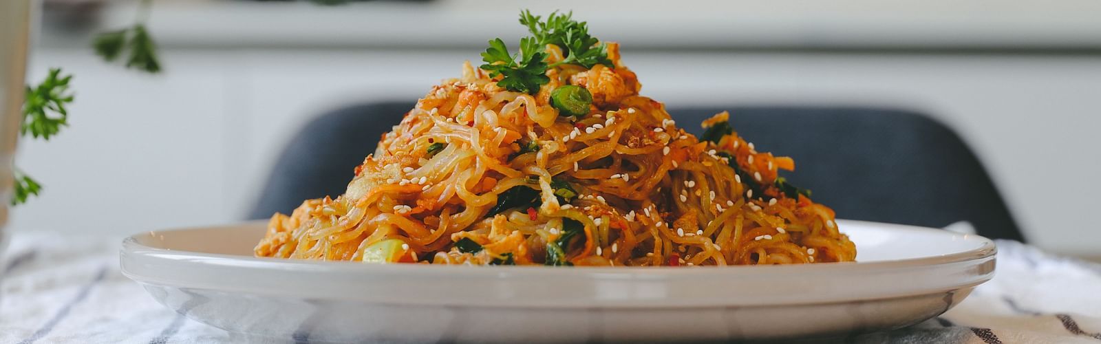 A plate consisting of Pad Thai placed on a table with a small plant in the background.