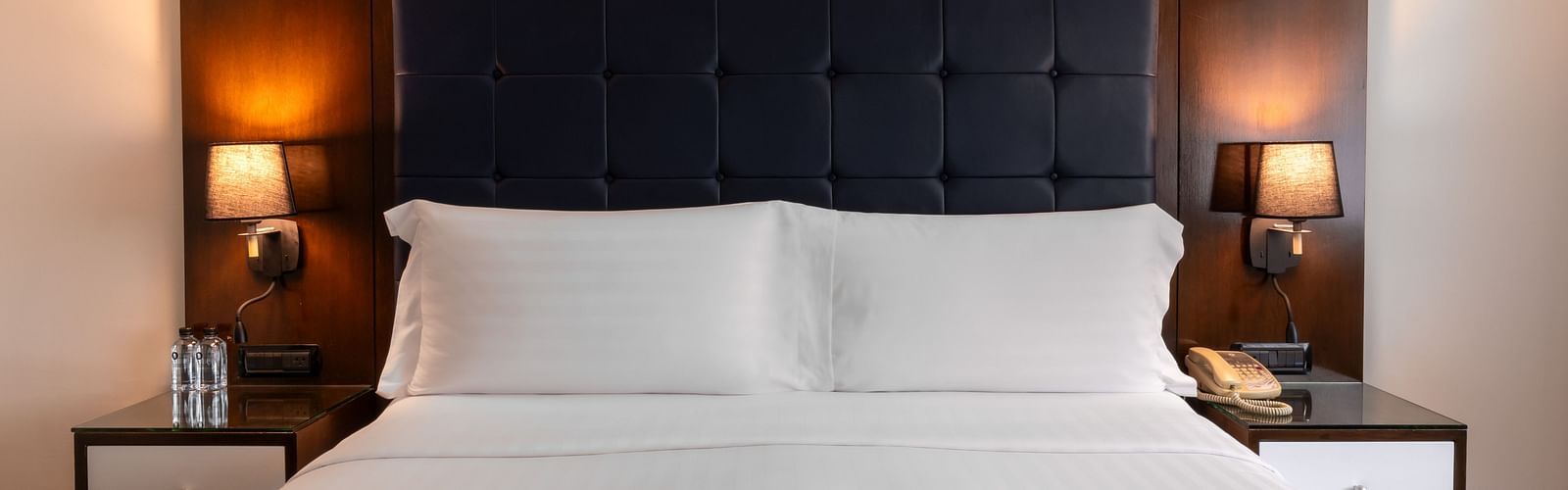A close up shot of a king bed with side tables and lamps - Night Hotel Bangkok.