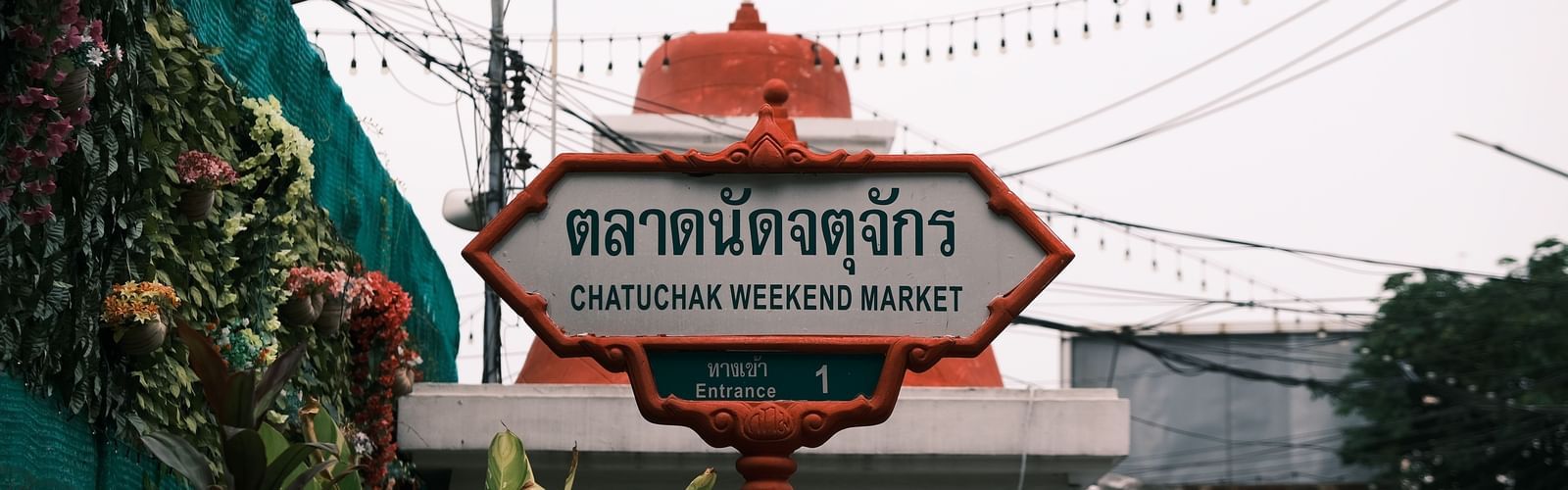 a signage of Chatuchak Weekend Market, Bangkok Famous Places to Visit, at the entrance of the event space with white clouds in the background.