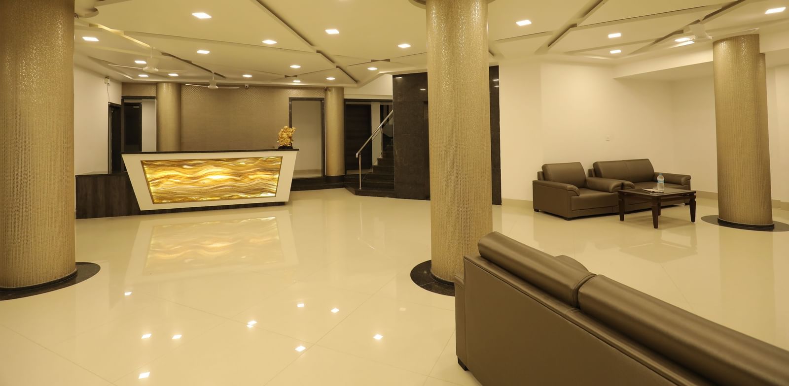 Lobby with golden pillars, polished floors, ceiling lights, and plush brown couches at Imperial Grande.
