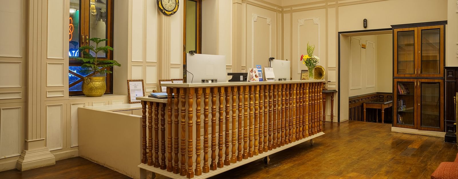 A reception desk at Orsino Spa Resort is made of light-coloured wood in a spacious room with ornate ceilings and chandeliers.