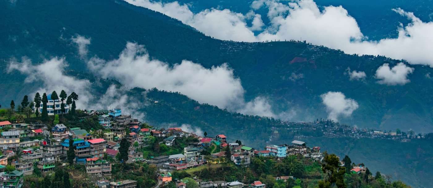 Hill town with colourful houses scattered across slopes, surrounded by mist-covered mountains.