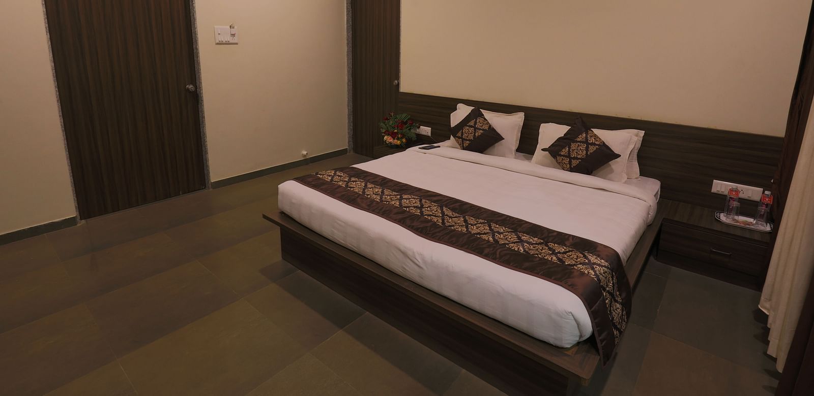 A bedroom with a double bed, dark wooden furniture, and a closed door - Vishal Lords Inn Gir Forest