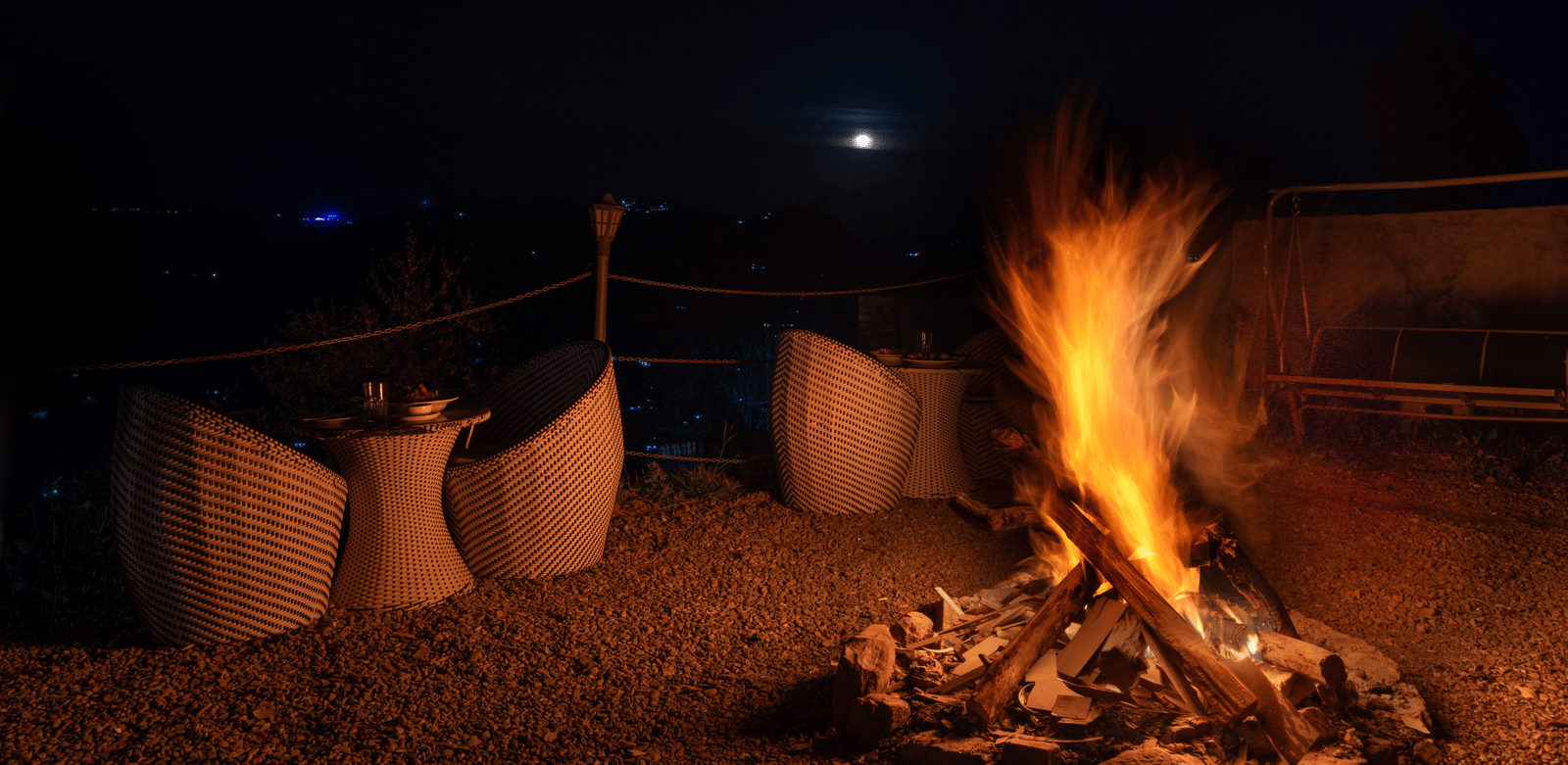 A glowing bonfire at night surrounded by comfortable outdoor chairs under a dark sky at Himalayas Resort By The Lake Hill, Mukteshwar.