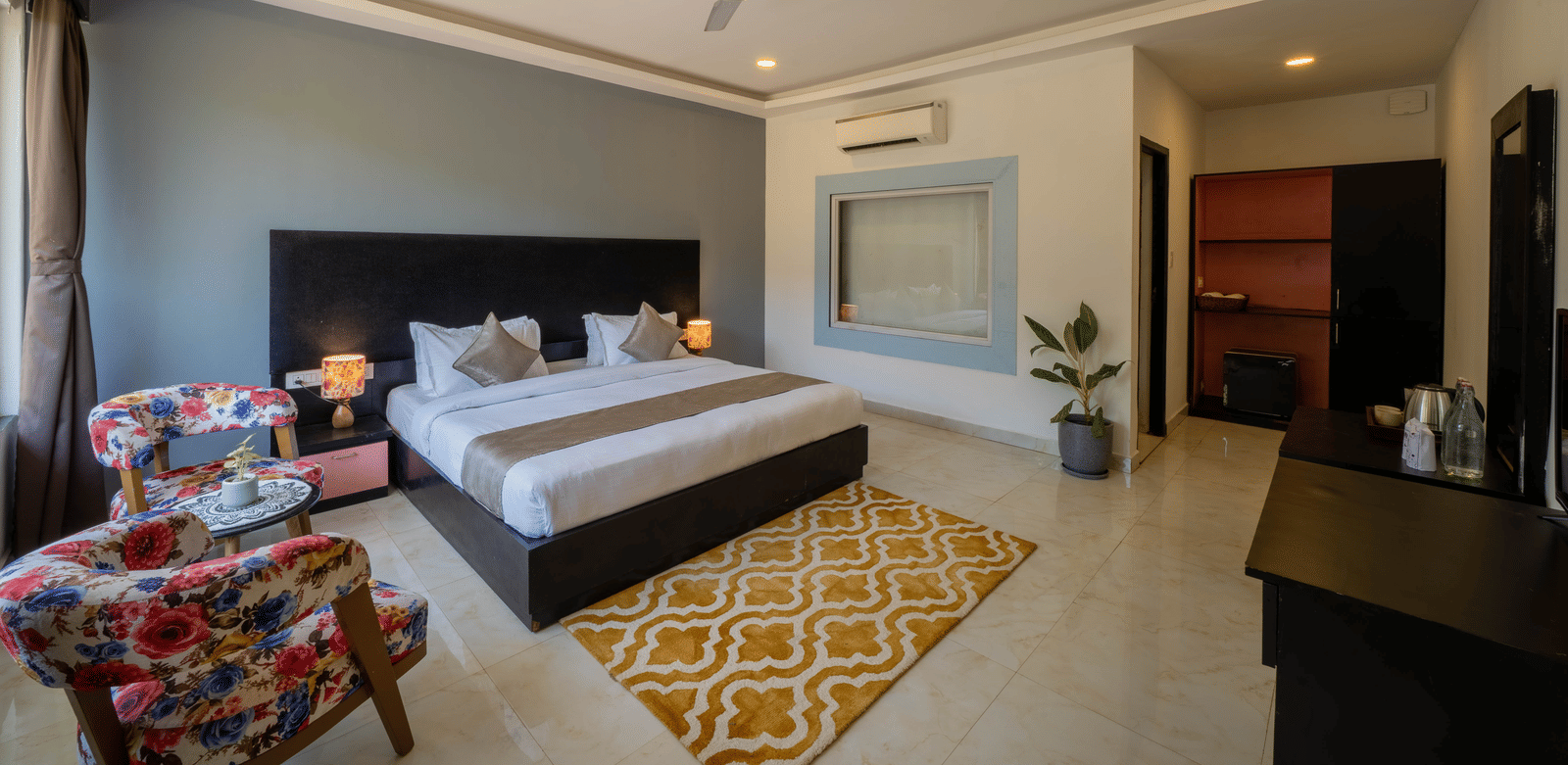 A room featuring a king size bed, air-conditioning, a potted plant, a desk with a TV above it, and a small seating area with 2 chairs and a coffee table - Perfectstayz Koko Maya