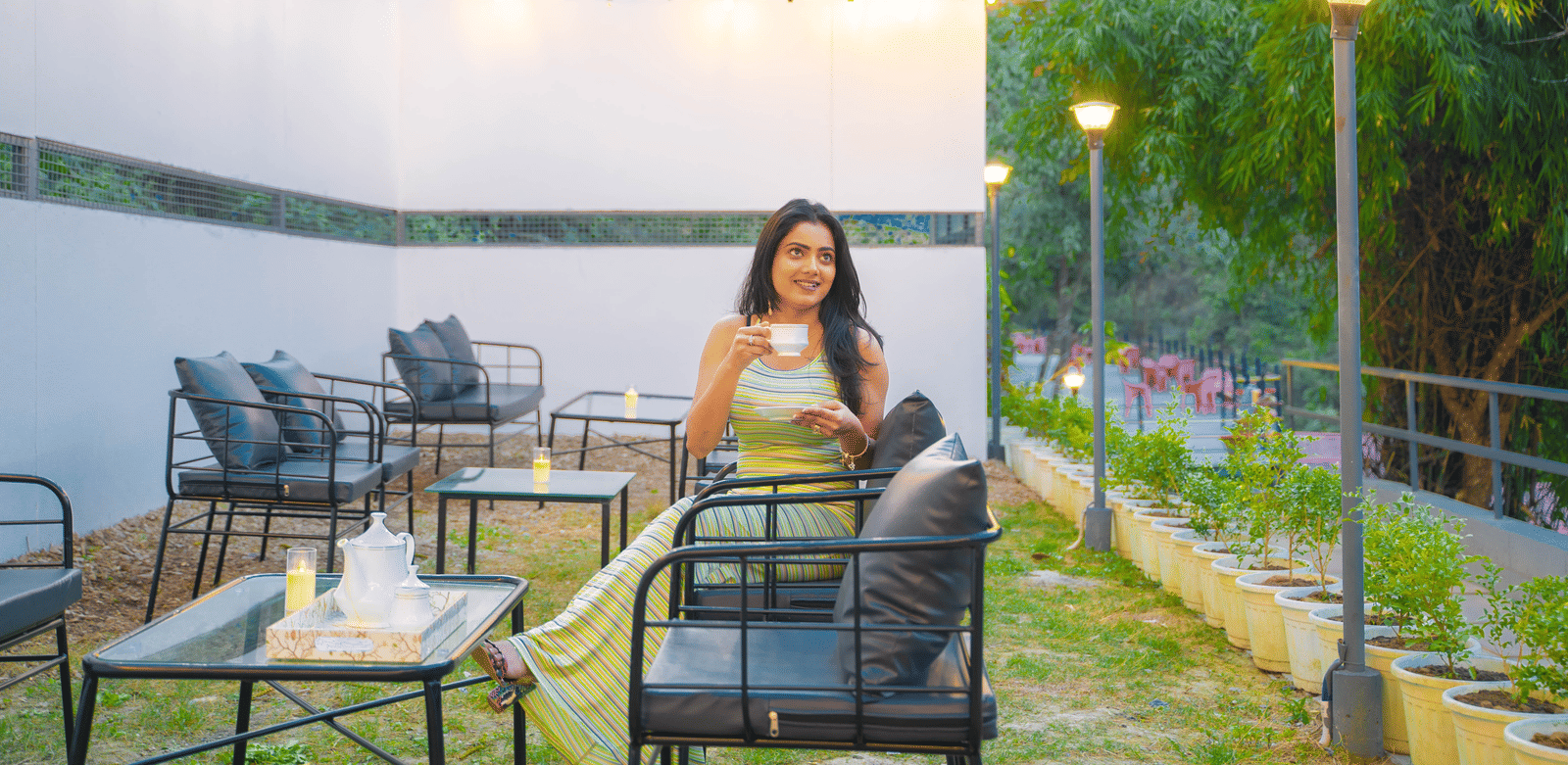 A person sits at an outdoor table at Perfect Stayz The Jungle Resort under string lights.