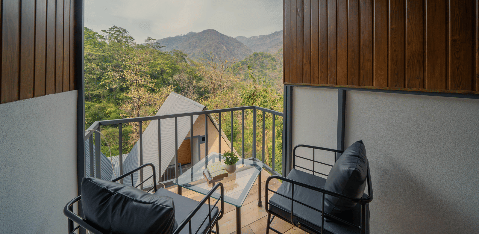 A balcony at Perfect Stayz The Jungle Resort has chairs and overlooks a mountain landscape.