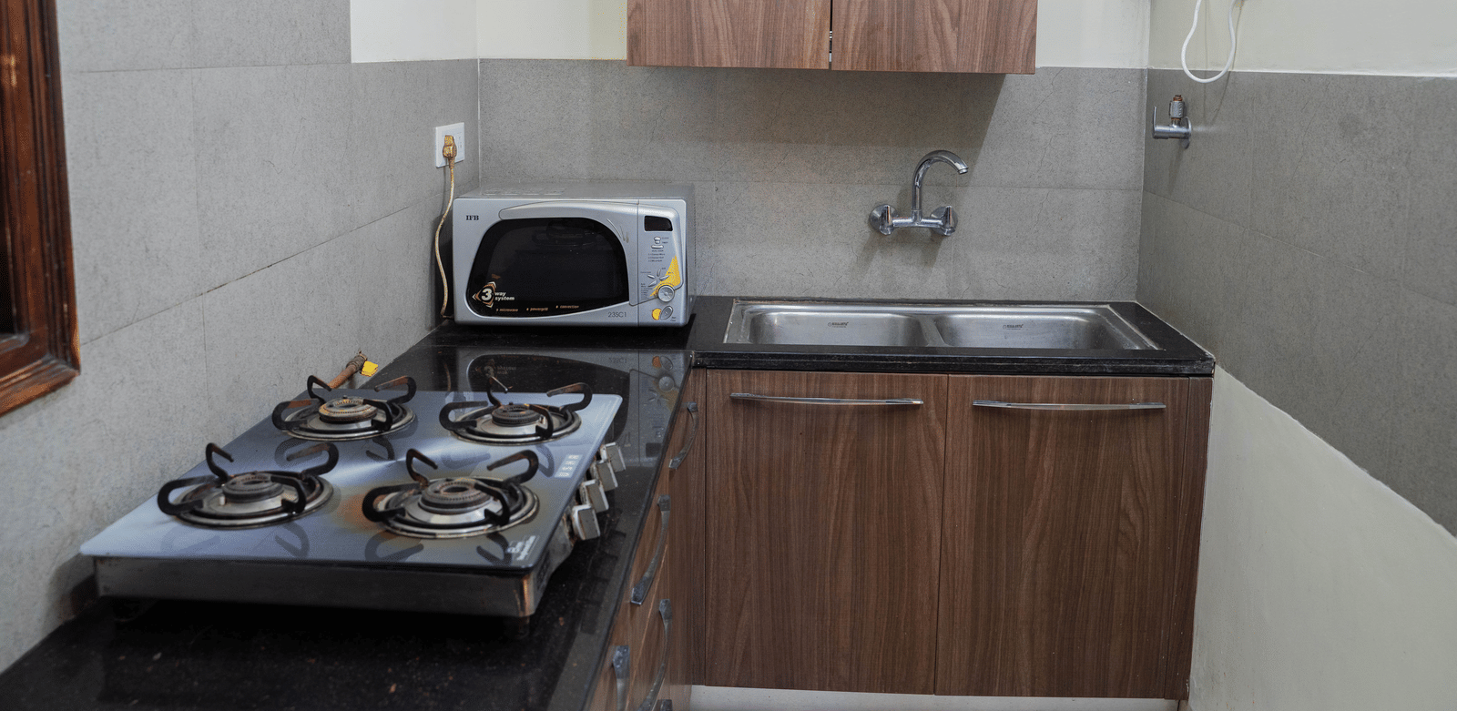 A kitchen area with a gas stove, microwave, sink, and wooden cabinets on a countertop against tiled walls at Perfectstayz Value Shimla (Namah Retreat).