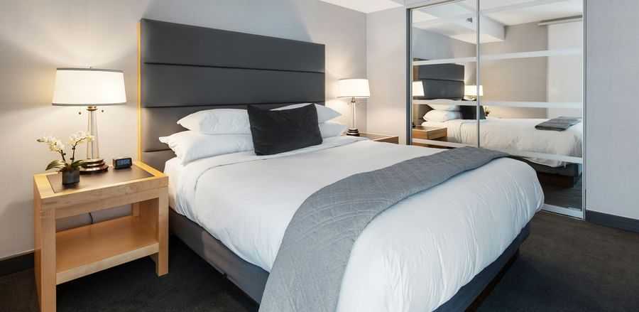 A modern hotel room with a double bed, a table with a lamp beside it and a huge mirror.