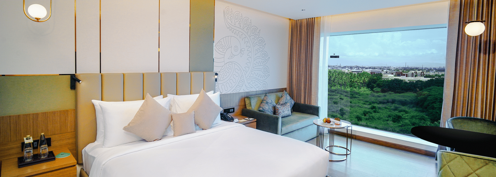 A bright, modern hotel room with a large bed, a comfortable sofa, and a wide window offering a view of lush greenery - Grand Madurai by GRT Hotels