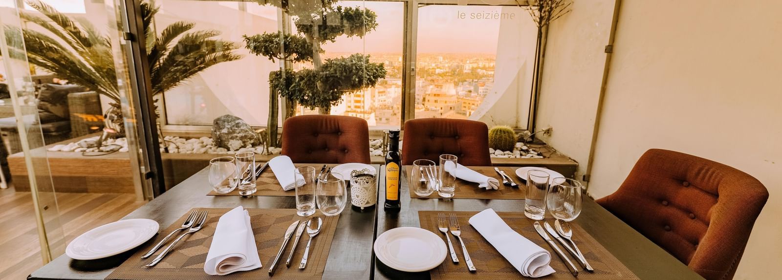 A well-arranged dining table with cutlery and glassware featuring mesmerising city views in the background beyond the glass panels on the terrace.