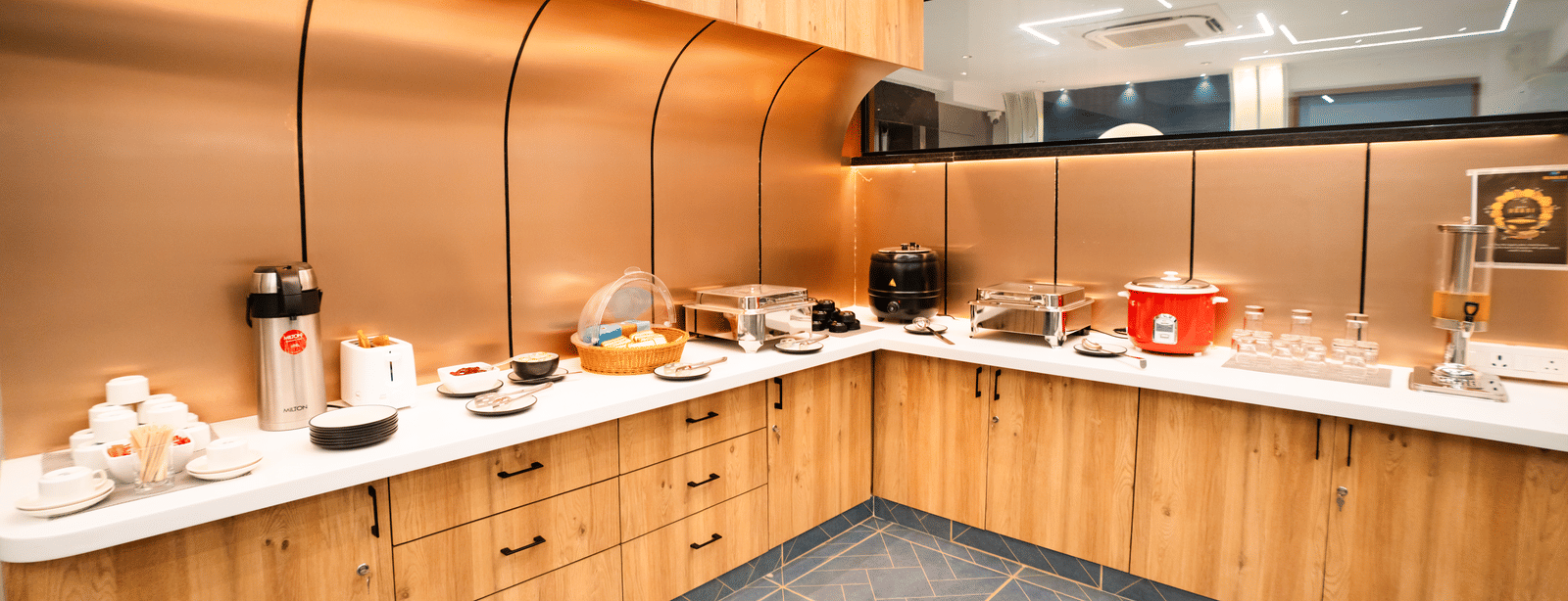 Dining area with buffet setup on an L-shaped counter featuring various dishes and cutlery at Sunrise Business Hotel, Hyderabad.