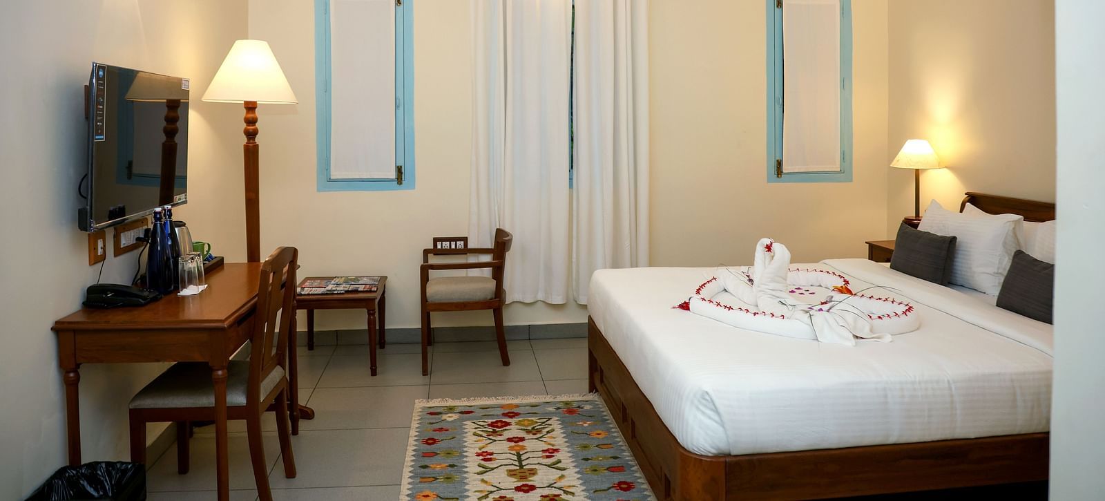 A suite with a large bed, flat screen TV, table and chair, and three lamps of different sizes | Mango Hill La Serene, Pondicherry