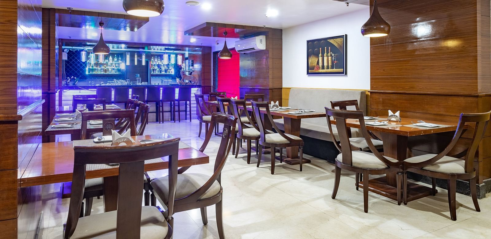 Modern restaurant at Diamond Palace Lords Plaza with wooden tables, chairs, pendant lights, and a bar area.