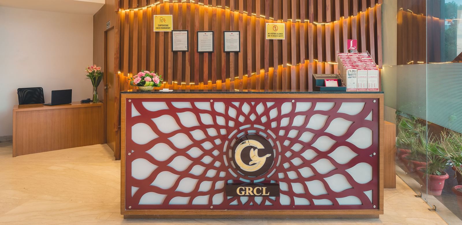 The reception area of Lords Inn Udaipur features a decorative front desk with a central logo, set against a wooden slat wall with framed displays.
