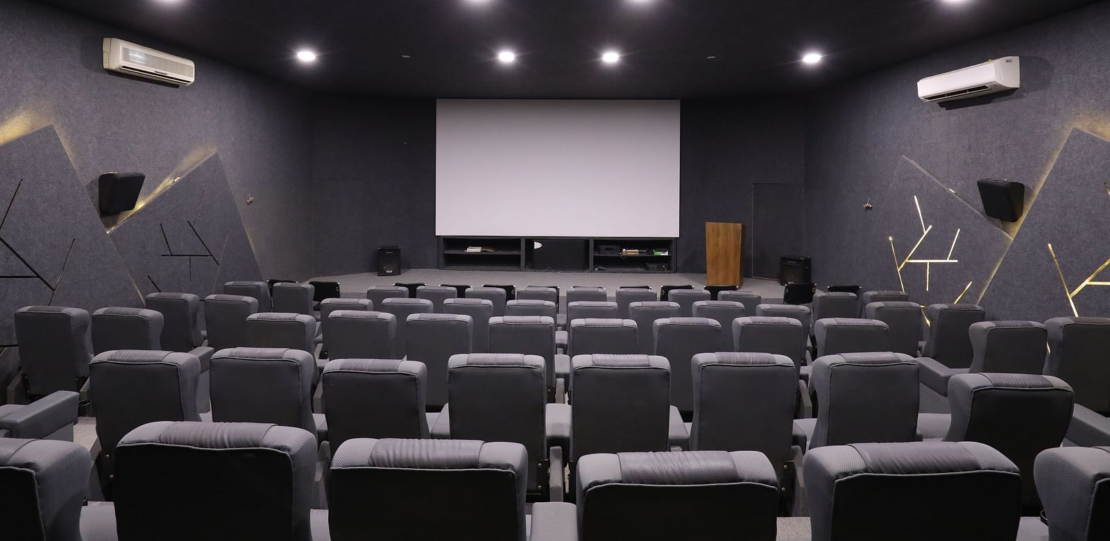 A private cinema room with rows of plush seating facing a large projection screen - Vishal Lords Inn Gir Forest