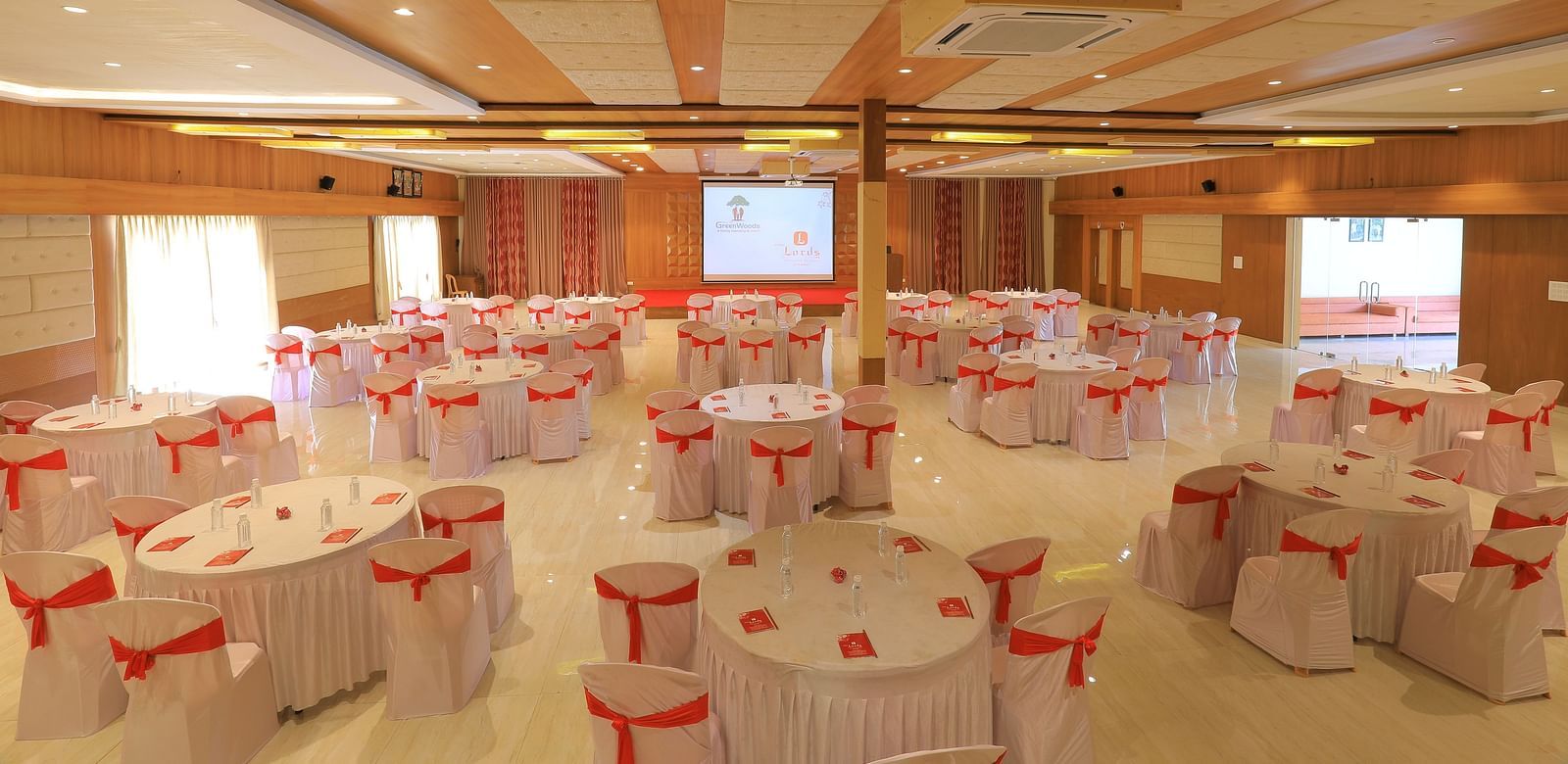 An expansive banquet hall with round tables draped in white and pink table cloth, ready for an event - Vishal Lords Inn Gir Forest