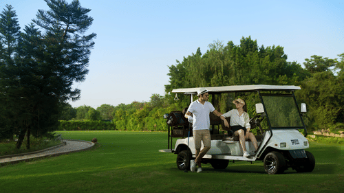 2 guests chatting with each other as they are placed on the golf cart, surrounded by a lush green lawn and trees at Heritage Village Resorts & Spa, Manesar, perfect for a luxury staycation near Gurgaon.