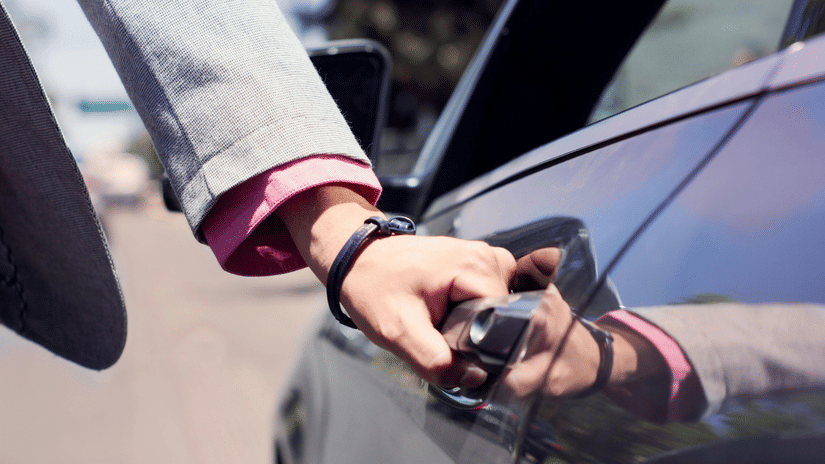 A person holding a car door handle, with part of the vehicle and road visible in the background.