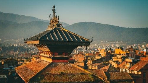 A multi-tiered pagoda roof with intricate details overlooking a cityscape and distant hills.