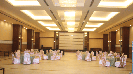 Decorated chairs and tables arranged in a circular format in a banquet hall at Pipul Padmaja Premium Hotel & Convention.