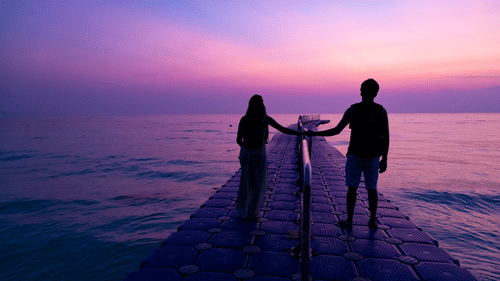 A couple posing for a picture during sunrise at Kalapathar Beach while standing on a man-made pier and looking at the sky.