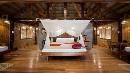 View of a wooden bedroom at Flower Island Resort with a white canopy bed and nightstands on both sides.