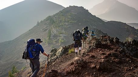 A group of hikers trekking along a rocky mountain trail with backpacks and trekking poles.