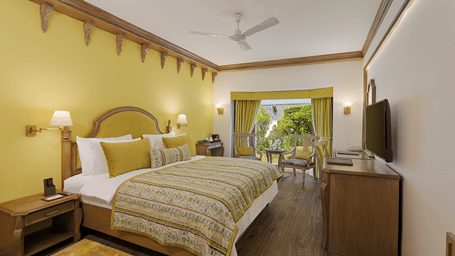 A room with a queen size bed with light linens, yellow accent walls, nightstands, wall-mounted television, and a desk area at Ramada by Wyndham Mussoorie Mall Road.