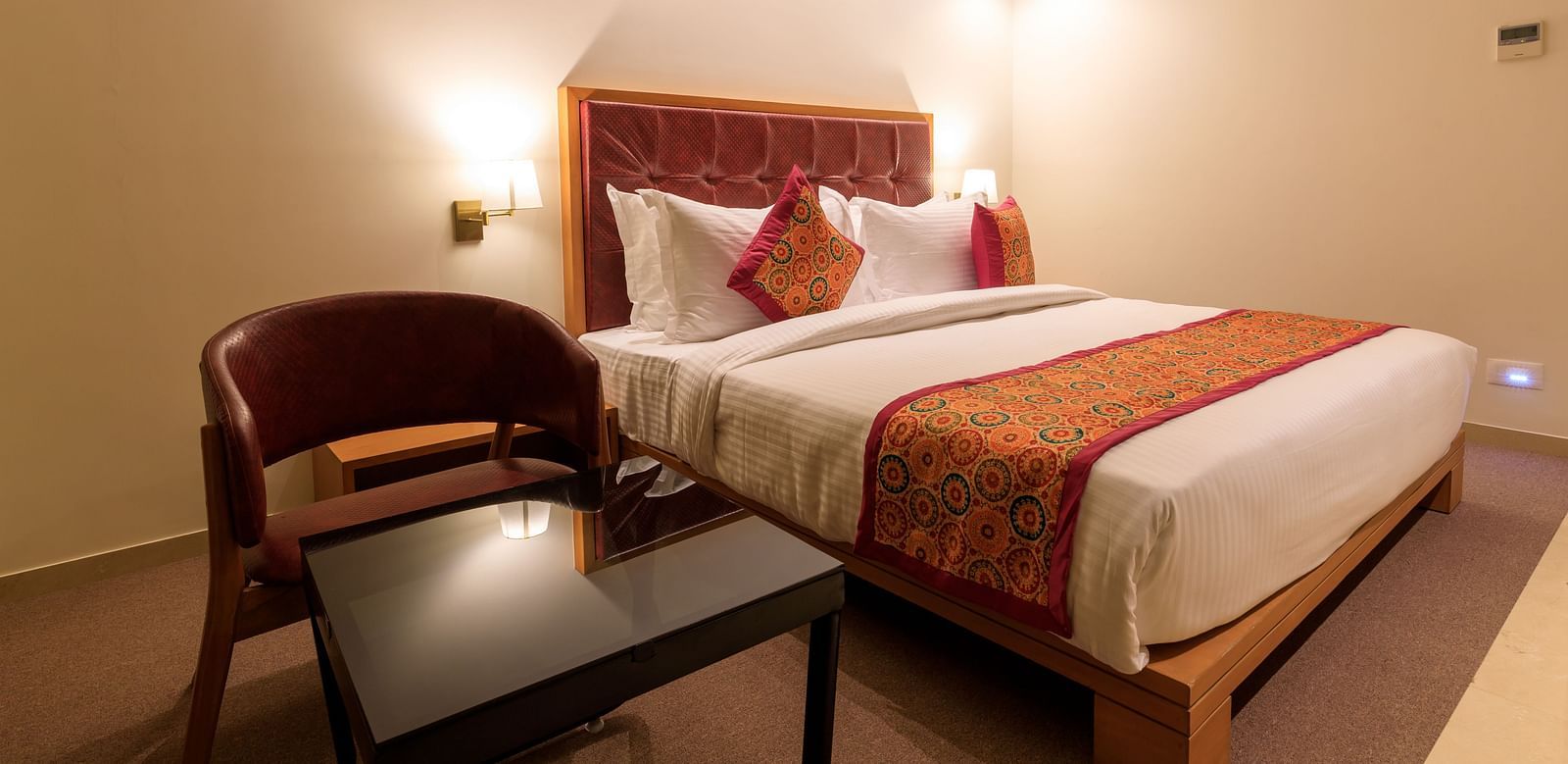 A warmly lit hotel room at Lords Eco Inn Apple Gate features a double bed with patterned accents, a chair and a small table.