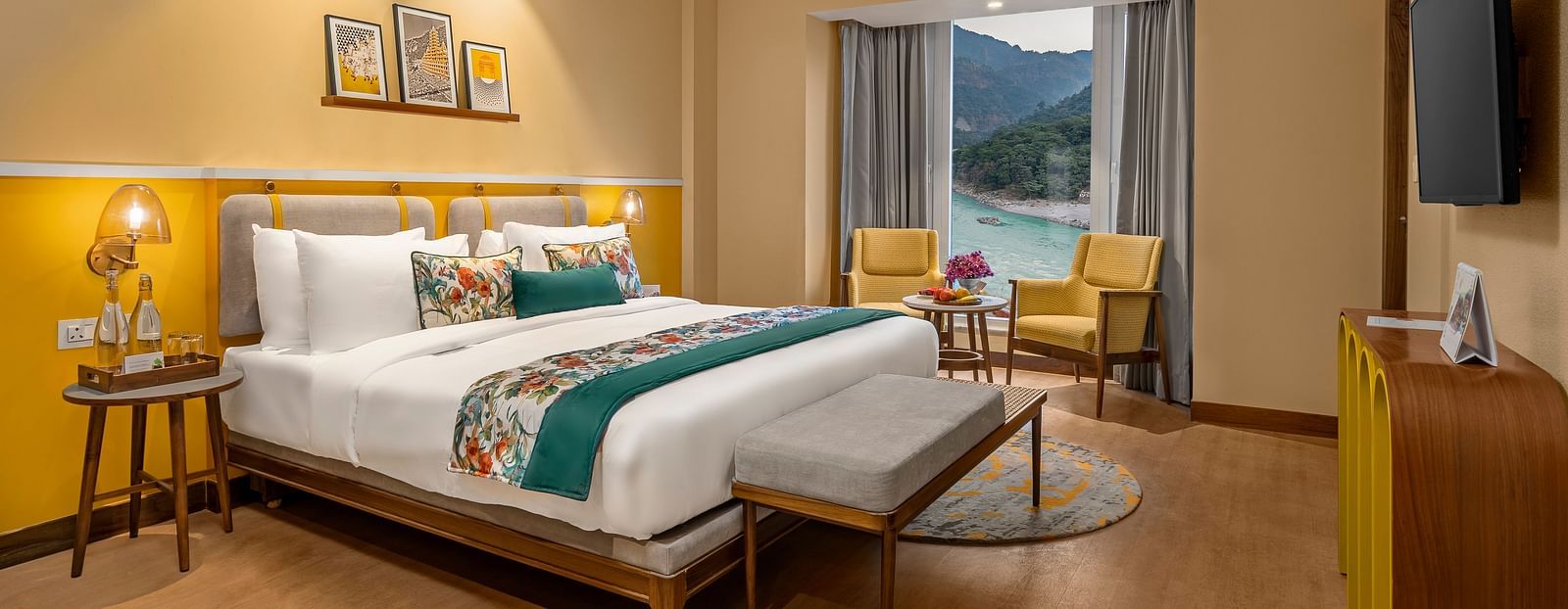  The room features a king-size bed with a plush headboard and comofrtable bedding. Armchairs by the window, offering a scenic view of the mountains. The room also includes a wooden desk, a television, and a ceiling fan. 