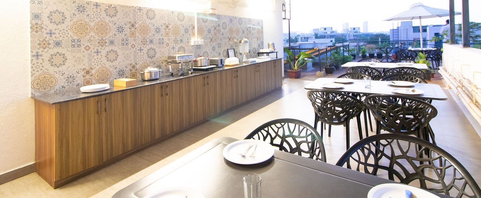 A dining space with tables and chairs under a partial roof, featuring a buffet setup along one side at Sanctum Suites Indiranagar, Bangalore.