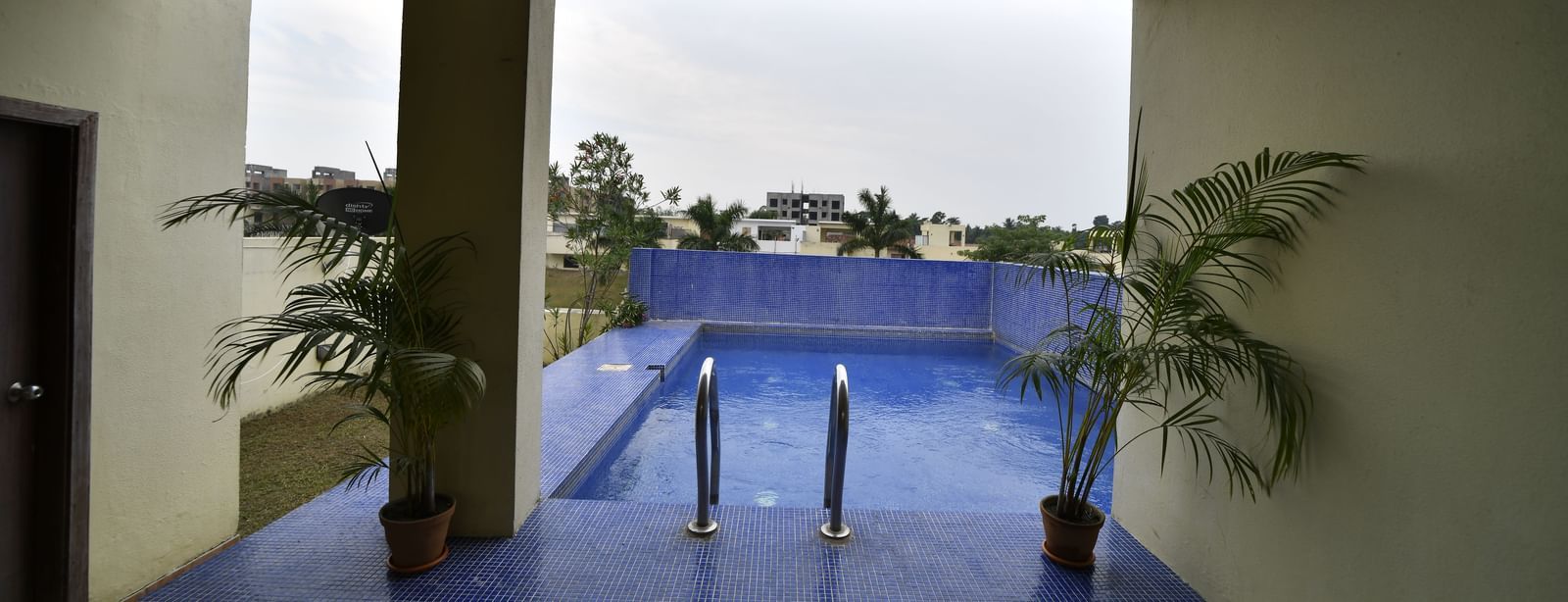 An open-air or covered patio area with a blue floor, potted plants, and a view of the sky and distant trees | Aqua Bungalow | Vedic Village Spa Resort, Kolkata