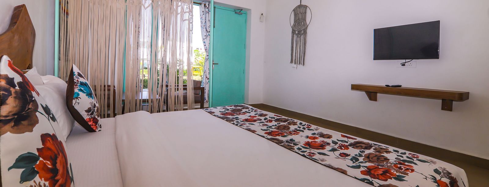 Interior of a guest room at Vedikant Resorts The Mallard Corbett with a large bed, cushioned chairs, a wall-mounted TV, and a glass door.