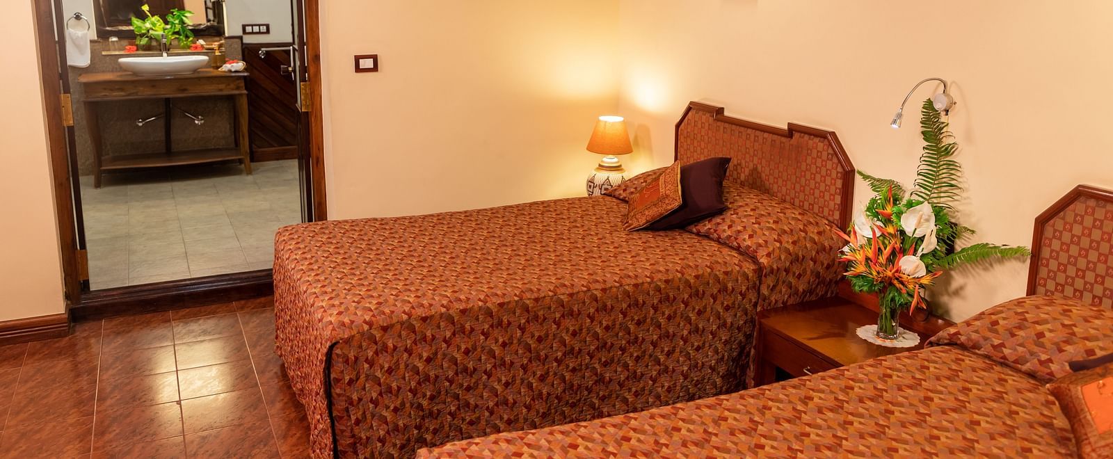 Cosy room with twin beds, warm lighting, and a glimpse into the bathroom - BluSalzz Collection - Tranquil Resort, Wayanad