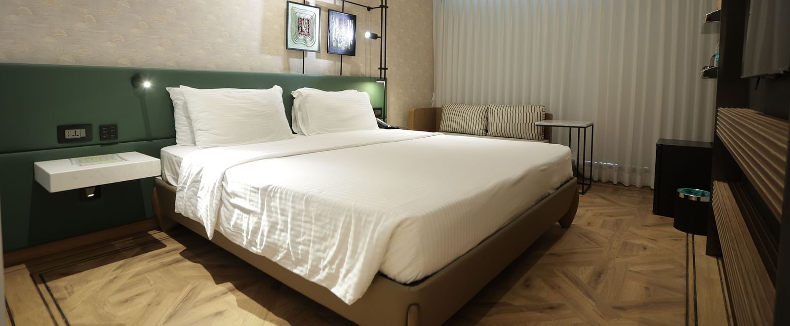 Modern guest room at Regency Hotel, Mumbai with plush bedding, contemporary furniture, large windows and elegant green accent wall for a comfortable stay.