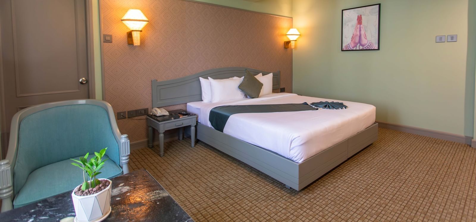  A hotel bedroom at Shilton International, Kochi, with a large bed, decorative wall sconces, and a comfortable armchair.