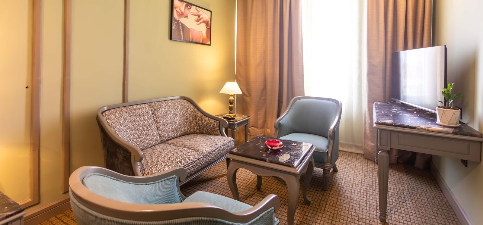  A sitting area at Shilton International, Kochi, with a sofa, two armchairs, and a well-lit window.