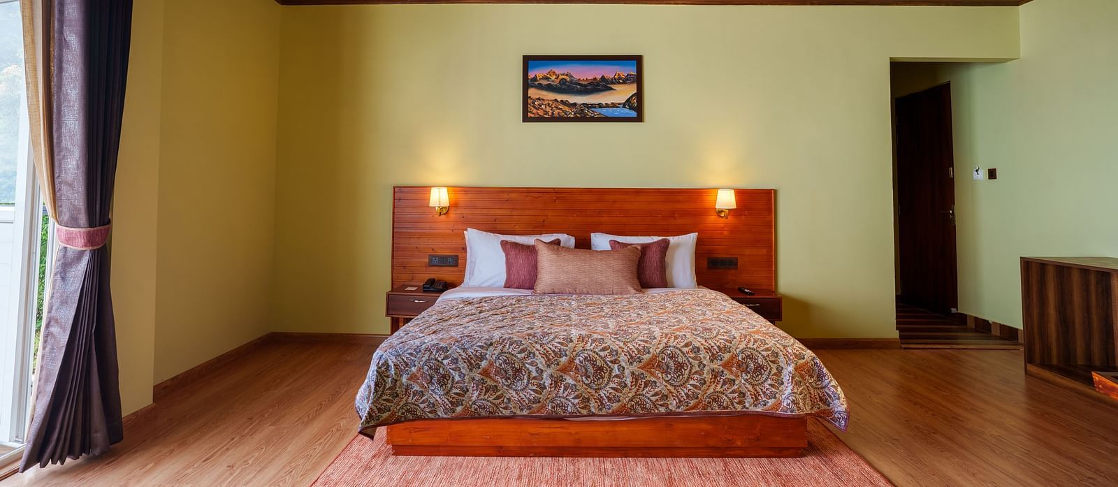 A well-appointed hotel bedroom featuring a bed with a wooden headboard, a TV, and a window, representing a typical guest room at Summit Enigma Resort and Spa.