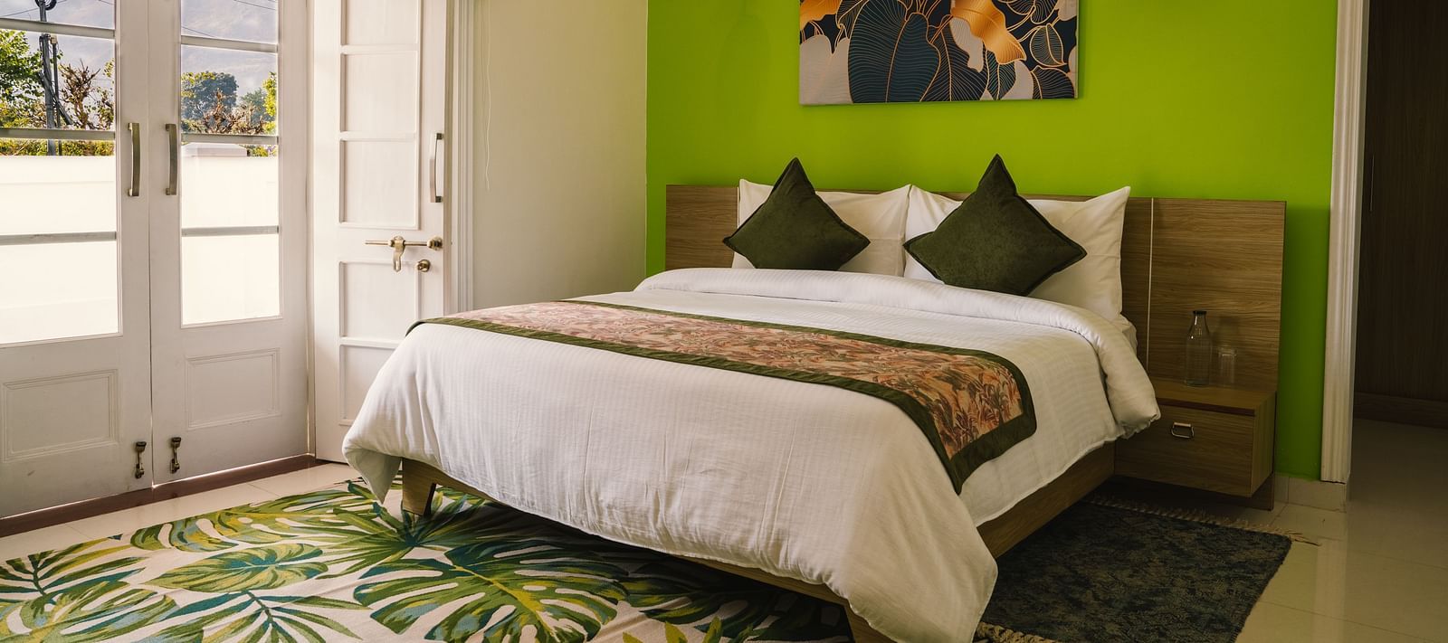 A spacious room at BluSalzz Villas - The Green Roof, Bhimtal featuring a large bed, a photo frame above the headboard, a carpet, and a door leading to the balcony.
