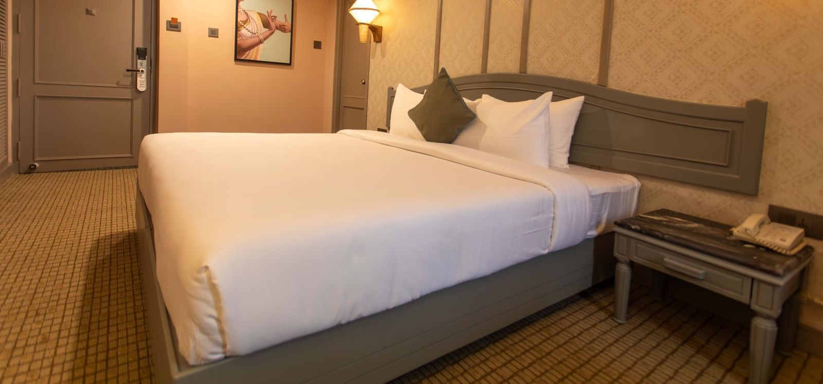 A bedroom at Shilton International, Kochi, with a large bed, stylish headboard, and elegant wall panelling.