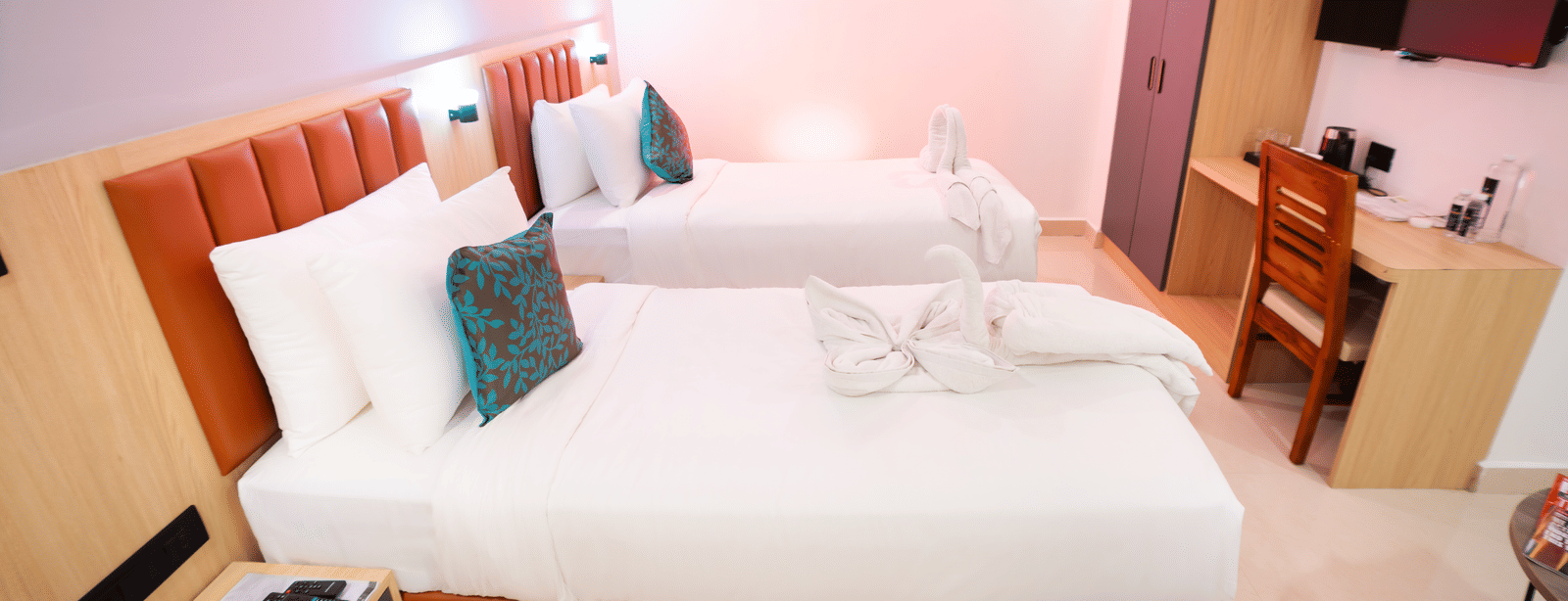 Side view of a spacious room with twin beds, a bedside table, and a wall-mounted television at Sunrise Business Hotel, Hyderabad.