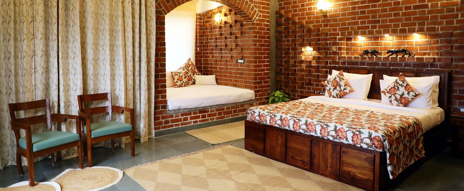 A bedroom at Tisya Farms, Gurgaon with a double bed, chairs, brick walls, curtains, and overhead lighting.