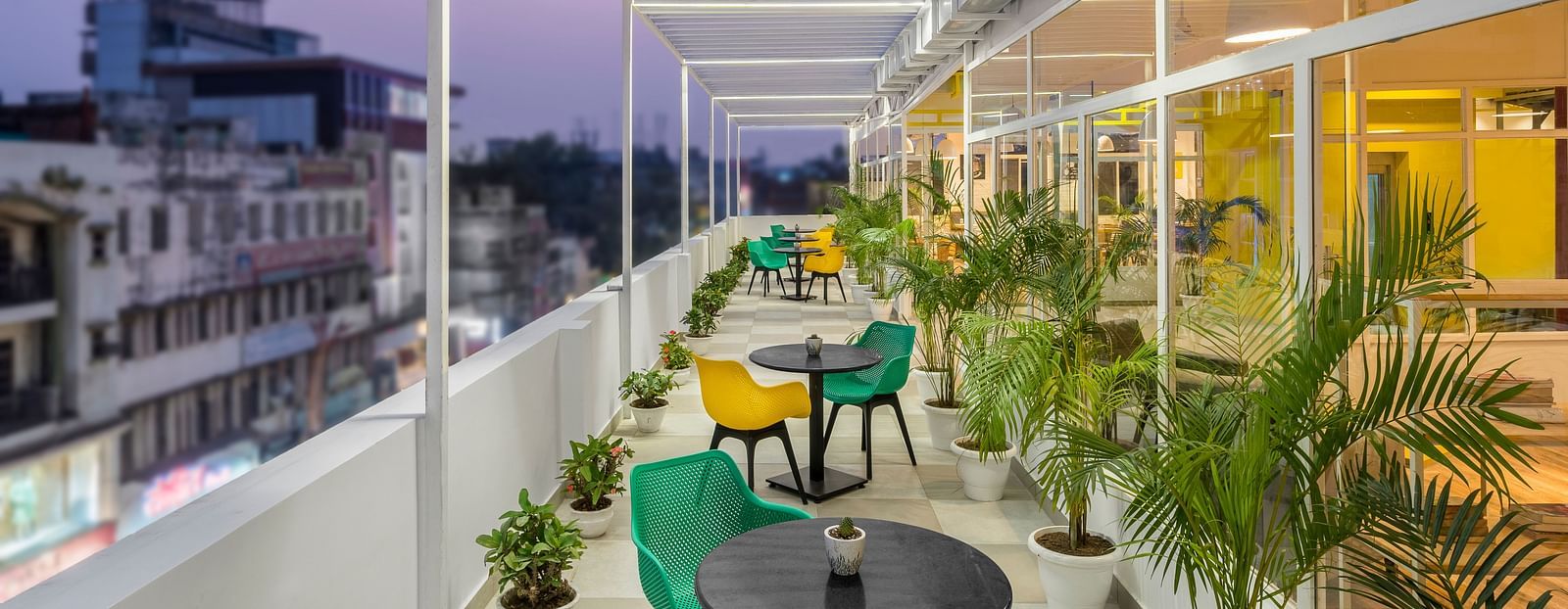 An image of a rooftop outdoor seating area featuring multiple chairs and tables, captured in the evening with lights illuminated.