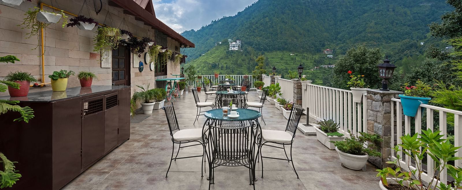 Rooftop dining area with mountain views under a cloudy blue sky, at BluSalzz Collection - Suvaasa Resort, Ramgarh.