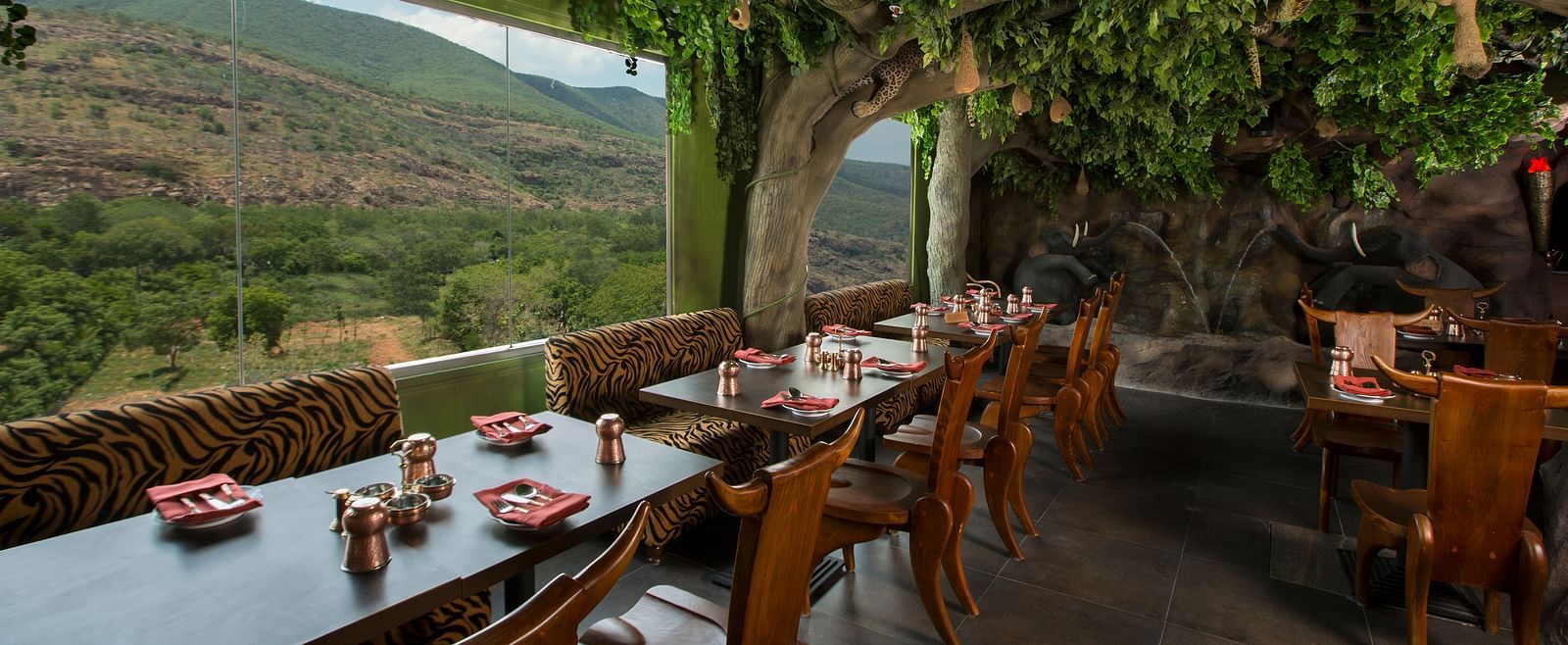 An image of a restaurant decorated with trees featuring several chairs and tables - The President Hotel, Hubli