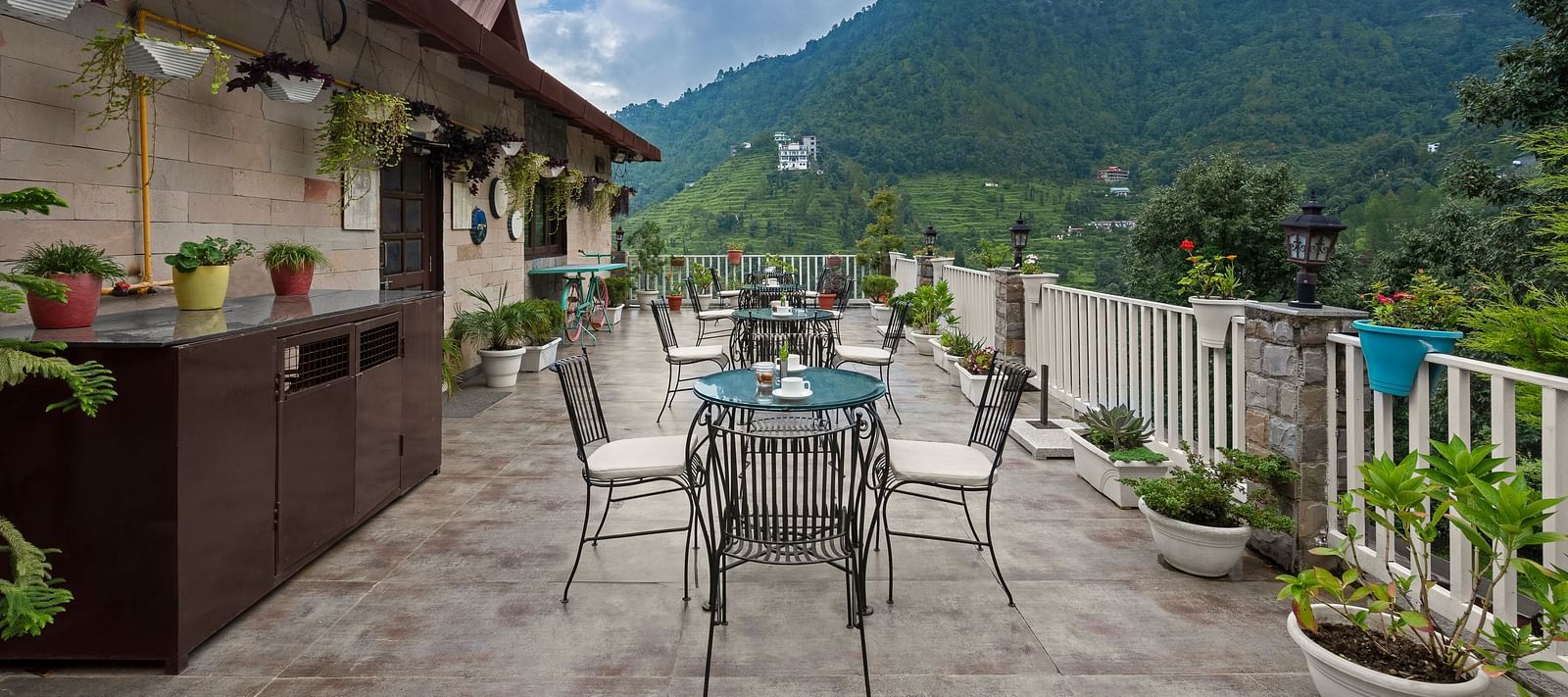 Rooftop dining area with mountain views under a cloudy blue sky, at BluSalzz Collection - Suvaasa Resort, Ramgarh.