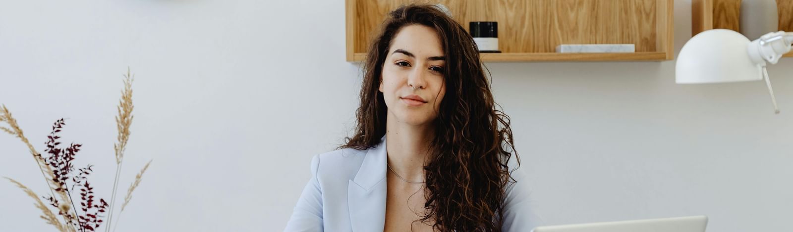 A businesswoman in a light blazer sitting at a desk with a laptop.