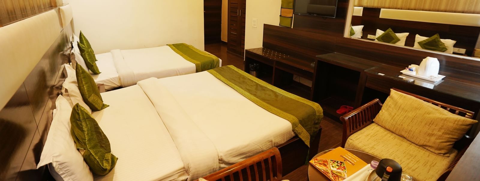 Family room with two King-sized beds, two chairs with centre table, wall-mounted TV and mirror, AC and kettle.